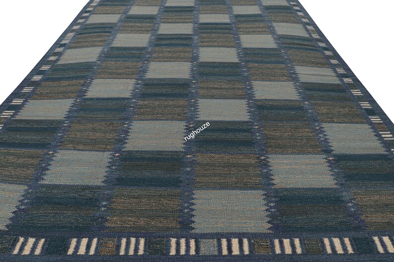 Puede incluir: Una alfombra rectangular con un patr&oacute;n de cuadros en tonos de azul, gris y marr&oacute;n. La alfombra tiene un borde con un dise&ntilde;o geom&eacute;trico repetitivo. La vista en perspectiva resalta la textura y el dise&ntilde;o de la alfombra.