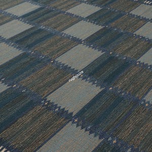 Puede incluir: Una alfombra tejida con un patr&oacute;n geom&eacute;trico. La alfombra presenta un dise&ntilde;o de tablero de ajedrez con cuadrados alternos azules y grises. La alfombra tiene una apariencia texturizada y un borde con rayas blancas.