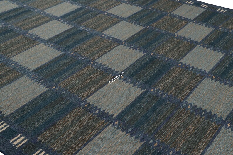 Puede incluir: Una alfombra tejida con un patr&oacute;n geom&eacute;trico. La alfombra presenta un dise&ntilde;o de tablero de ajedrez con cuadrados alternos azules y grises. La alfombra tiene una apariencia texturizada y un borde con rayas blancas.