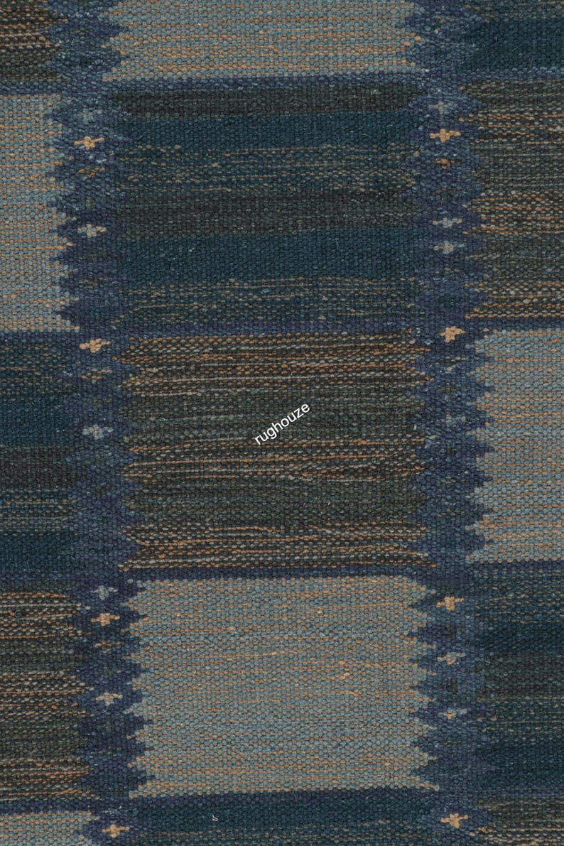 Puede incluir: Primer plano de una alfombra tejida con un patr&oacute;n geom&eacute;trico. La alfombra presenta un dise&ntilde;o repetitivo de cuadrados y rect&aacute;ngulos en tonos de azul, marr&oacute;n y gris. La textura de la alfombra es visible, con un aspecto ligeramente &aacute;spero. La palabra "rughouze" est&aacute; impresa en la alfombra.