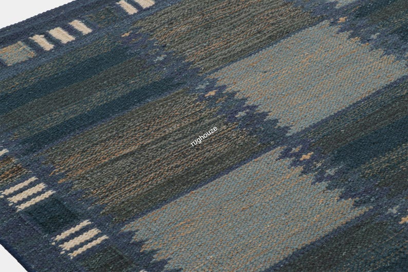 Puede incluir: Primer plano de una alfombra tejida azul y beige con un patr&oacute;n de rayas. La alfombra presenta bandas alternas de azul oscuro, azul claro y beige. Los bordes tienen un borde decorativo con rayas blancas. La alfombra est&aacute; hecha de un material texturizado.