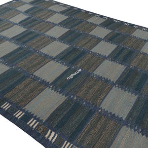 Puede incluir: Una alfombra rectangular grande con un patr&oacute;n de cuadros en tonos de azul, gris y marr&oacute;n. El dise&ntilde;o presenta cuadrados alternos de diferentes tonos, creando un efecto geom&eacute;trico. El borde tiene un patr&oacute;n de rayas en blanco y azul.