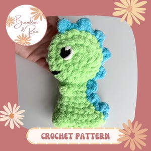 以下が含まれることがあります： 緑と青の恐竜のおもちゃの編み物パターン。恐竜は黒い目と小さな口でかわいい顔をしています。パターンは購入できます。