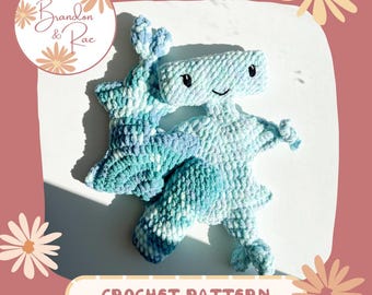 May include: A crochet pattern for a blue and green crocheted robot toy. The robot has a smiling face and is standing on a white surface. The pattern is available for purchase from Brandon & Rae.