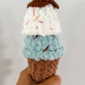 Peut inclure: Un jouet en forme de cornet de glace crochet&eacute; avec trois boules de glace. La boule du haut est blanche avec des p&eacute;pites color&eacute;es, la boule du milieu est bleu clair et la boule du bas est brune.