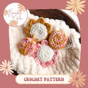 May include: Crochet pattern for a set of four amigurumi toys: a sunflower, a ladybug, a snail, and a flower. The toys are made with white, pink, and yellow yarn and are sitting on a white fluffy blanket.