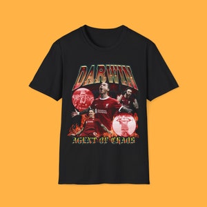 Puede incluir: Camiseta negra con un estampado gráfico de un jugador de fútbol celebrando un gol. El gráfico incluye el texto "DARWIN AGENT OF CHAOS" en un estilo retro.