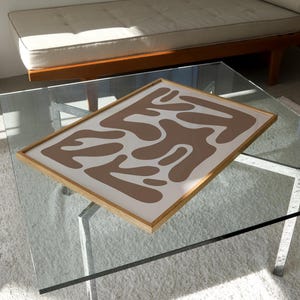 May include: A framed abstract print with a brown and white design. The print features a series of organic shapes that resemble abstract forms.