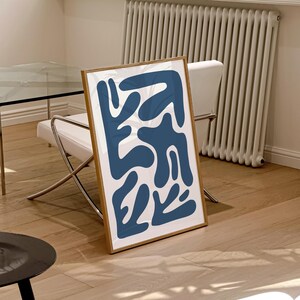 May include: A framed abstract print with a white background and blue abstract shapes. The print is in a wooden frame.