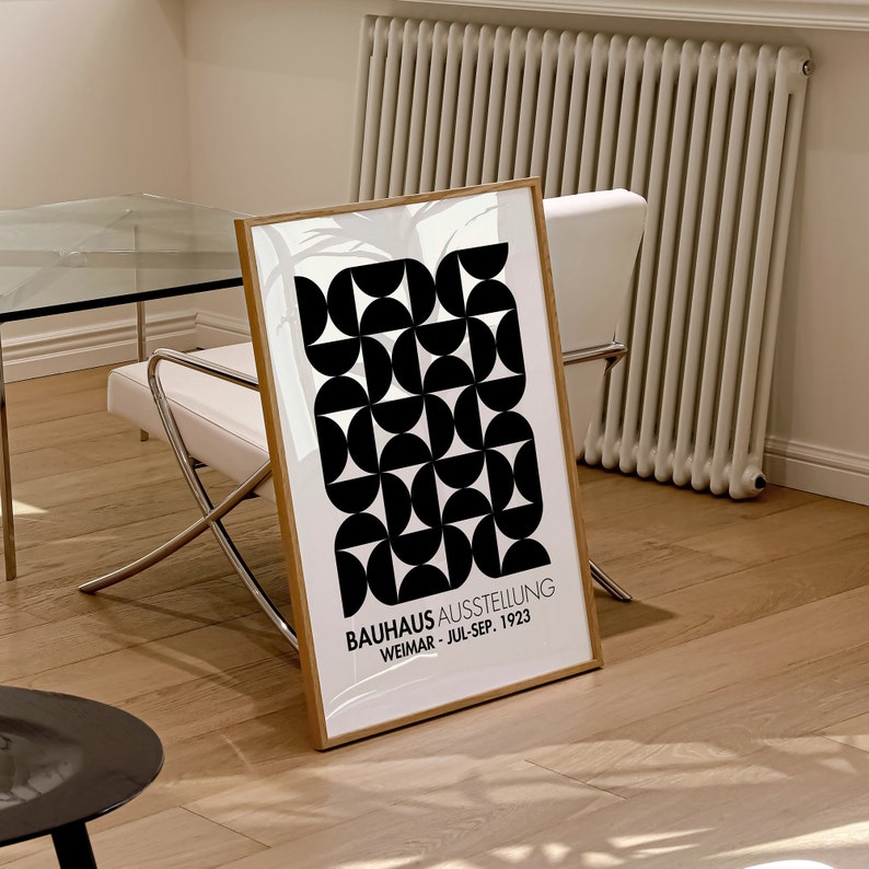 May include: A black and white geometric print poster in a wooden frame. The poster features a repeating pattern of circles and semi-circles. The text on the poster reads "BAUHAUS AUSSTELLUNG WEIMAR - JUL-SEP. 1923".