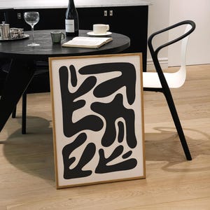 May include: A framed black and white abstract art print with a wooden frame. The print features a design of black shapes on a white background.