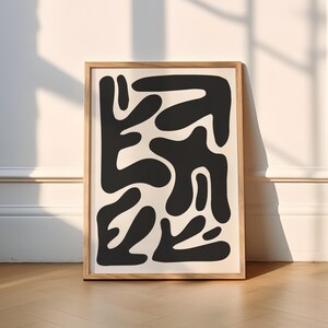 May include: A black and white abstract art print with a geometric design of organic shapes. The print is framed in a natural wood frame.