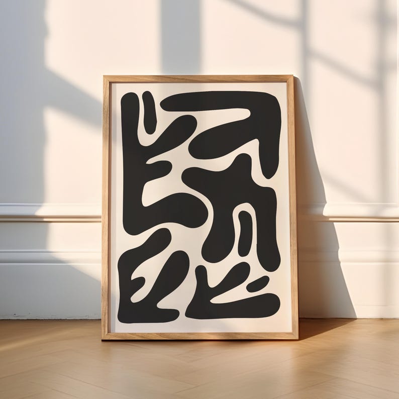 May include: A black and white abstract art print with a geometric design of organic shapes. The print is framed in a natural wood frame.