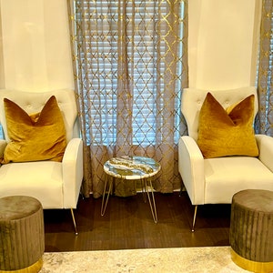 Könnte beinhalten: Zwei weiße Stühle mit goldenen Beinen und senfgelben Kissen, ein kleiner runder Tisch mit Marmorplatte und goldenen Beinen sowie zwei braune Hocker mit goldenen Verzierungen.