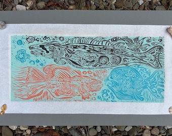 May include: A print featuring three stylized fish in black, coral, and blue on a light blue background. The artwork is on white paper, with seashells in each corner. The fish are intricately detailed.