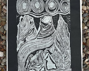 May include: A black and white linocut print depicting a mountain landscape with stylized peaks and swirling lines. Above the mountains are four circular shapes. The print is on a white-edged black paper.