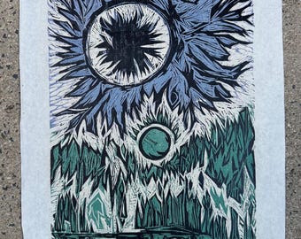 May include: A linocut print featuring a surreal landscape with a large, stylized sun and a smaller green orb. The artwork uses shades of blue, green, and black, with a textured, hand-printed aesthetic. The print is on a white paper.