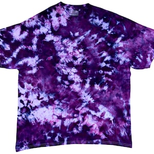 May include: A short-sleeve t-shirt featuring a tie-dye pattern in various shades of deep purple, violet, and light lavender. The fabric displays a swirling, mottled design with dark saturated areas contrasting against lighter, softer purple patches.