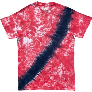 Puede incluir: Una camiseta de manga corta con cuello redondo y un patrón tie-dye en tonos rojos y blancos, con una franja diagonal prominente de color azul marino oscuro que va desde la parte inferior izquierda hasta la parte superior derecha. La etiqueta muestra la talla M.