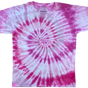 May include: A short-sleeve crew neck t-shirt featuring a vibrant pink and white spiral tie-dye pattern. The garment has a circular swirl design radiating from the centre, with varying shades of magenta and soft pink against a white background.