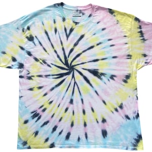 Puede incluir: Una camiseta de manga corta con un patrón de teñido anudado en espiral en tonos pastel de azul claro, rosa suave y amarillo pálido, acentuado con rayas de color negro carbón oscuro que irradian desde el centro hacia los bordes.