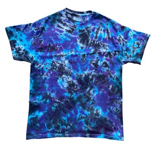 May include: A crew neck tie-dye t-shirt in blue, purple, and black. The short-sleeved shirt features a swirling tie-dye pattern. The design incorporates a mix of light and dark shades of the colors.