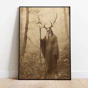 May include: Sepia-toned framed print featuring a figure in a forest. The figure wears a skull mask with large antlers, a long robe, and holds a staff. The background shows a misty forest with trees and ferns, creating a mystical atmosphere.