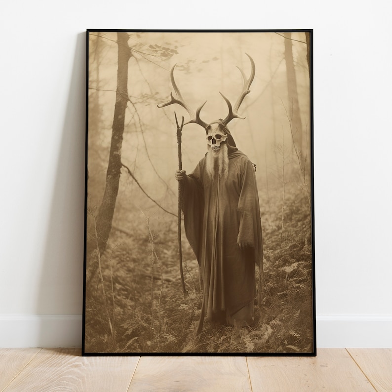 May include: Sepia-toned framed print featuring a figure in a forest. The figure wears a skull mask with large antlers, a long robe, and holds a staff. The background shows a misty forest with trees and ferns, creating a mystical atmosphere.