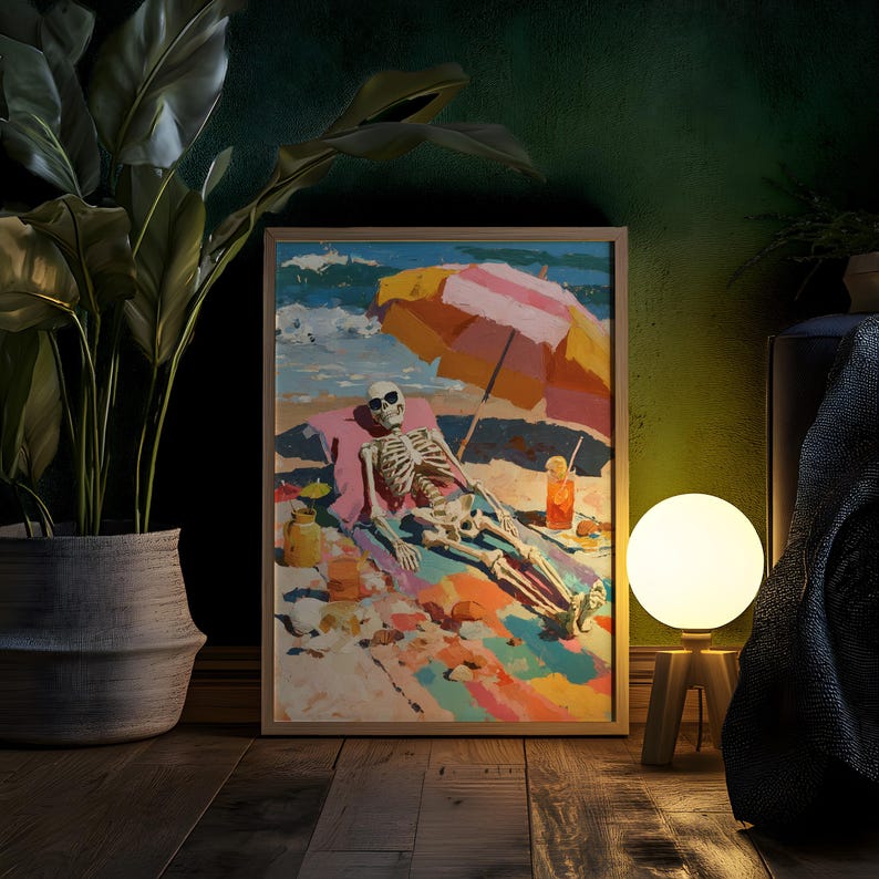May include: A framed art print depicts a skeleton relaxing on a beach under a striped umbrella. The artwork features vibrant colors, including blue, pink, yellow, and orange. A cocktail and other beach items are also visible. The print is displayed on a wooden floor.