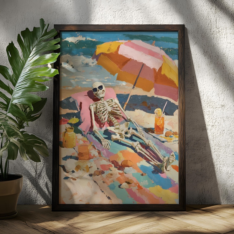 May include: A framed art print depicts a skeleton relaxing on a beach under a striped umbrella. The skeleton wears sunglasses and is lounging on a colorful beach towel. A drink with a straw and a small jar are also visible. The artwork is framed in a dark wooden frame.