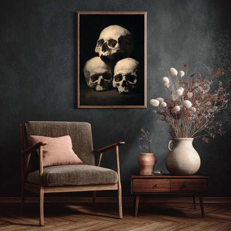 Pu&ograve; includere: Un'opera d'arte incorniciata raffigurante tre teschi umani in uno stile cupo e malinconico. I teschi sono impilati, con un focus sulla loro struttura ossea e sulle ombre. L'opera &egrave; sopra una sedia moderna con un cuscino rosa.