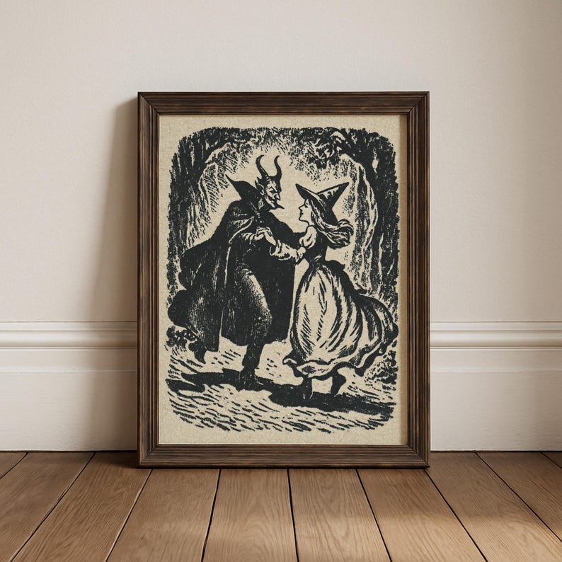May include: Framed black and white print showing a devil and a witch dancing in a forest setting. The devil is wearing a cape and has horns, while the witch wears a pointed hat and a long dress. The artwork is in a vintage style.