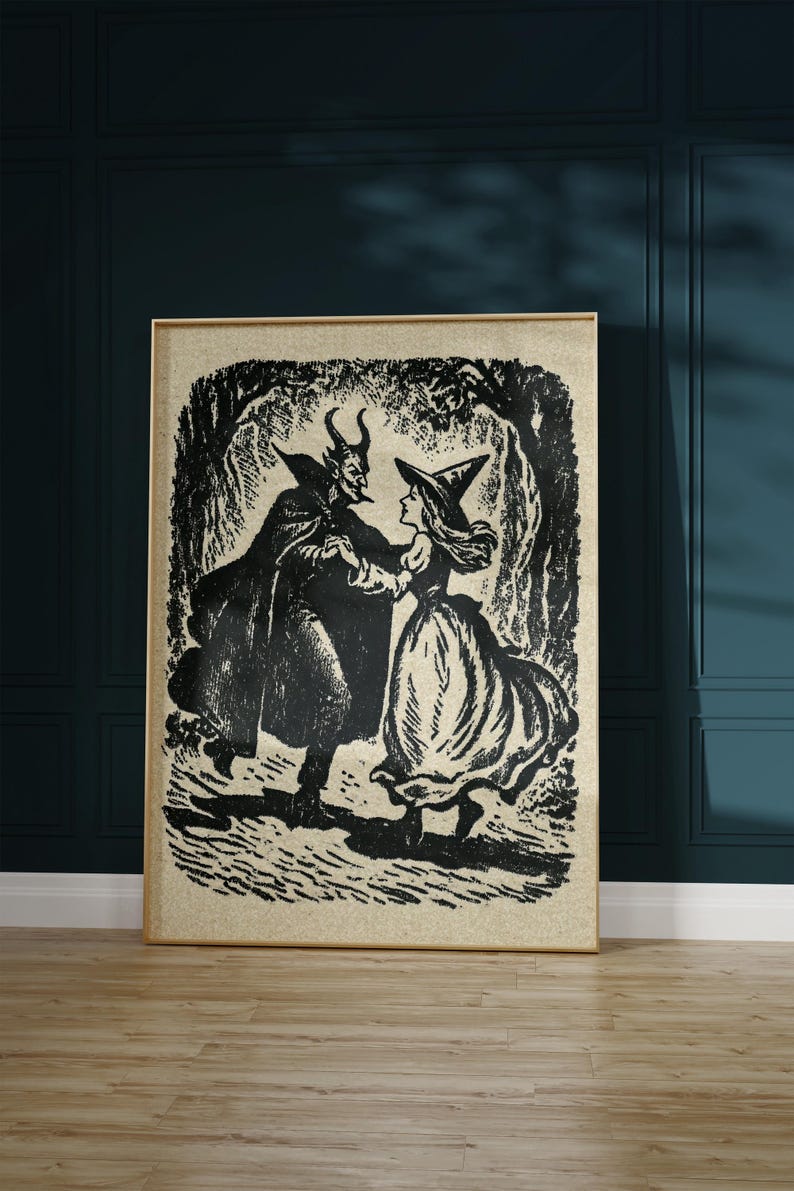 May include: A framed black and white vintage print depicting a devil and a witch dancing in a forest setting. The artwork is in a gold-coloured frame, set against a dark teal wall. The illustration style is reminiscent of classic Halloween imagery.