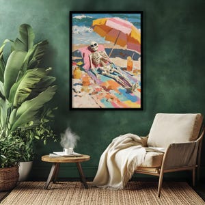 May include: A framed art print depicts a skeleton sunbathing on a beach under a striped umbrella. The artwork features vibrant colors, including blue, pink, yellow, and orange. The skeleton wears sunglasses and is lounging on a colorful beach towel.