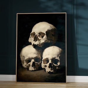 Pu&ograve; includere: Un'opera d'arte incorniciata con una natura morta di tre teschi umani. I teschi sono dipinti in tonalit&agrave; di bianco e beige su uno sfondo scuro. L'opera d'arte &egrave; esposta su una parete con pannelli blu scuro.