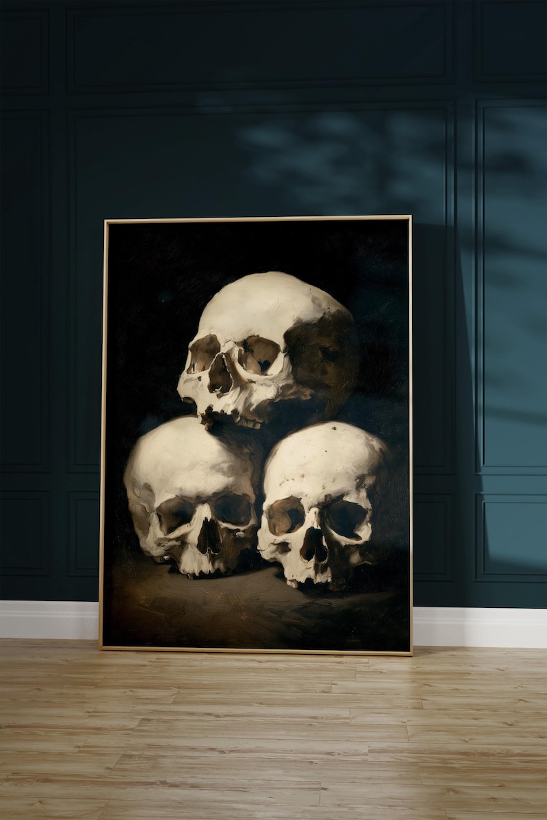 Pu&ograve; includere: Un'opera d'arte incorniciata con una natura morta di tre teschi umani. I teschi sono dipinti in tonalit&agrave; di bianco e beige su uno sfondo scuro. L'opera d'arte &egrave; esposta su una parete con pannelli blu scuro.