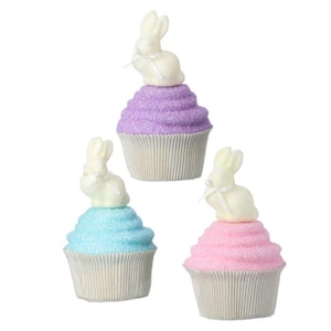 May include: Three decorative Easter cupcakes with pastel-colored frosting: purple, blue, and pink. Each cupcake is topped with a white bunny figurine and set in a fluted paper cup. A festive and colorful Easter decoration.