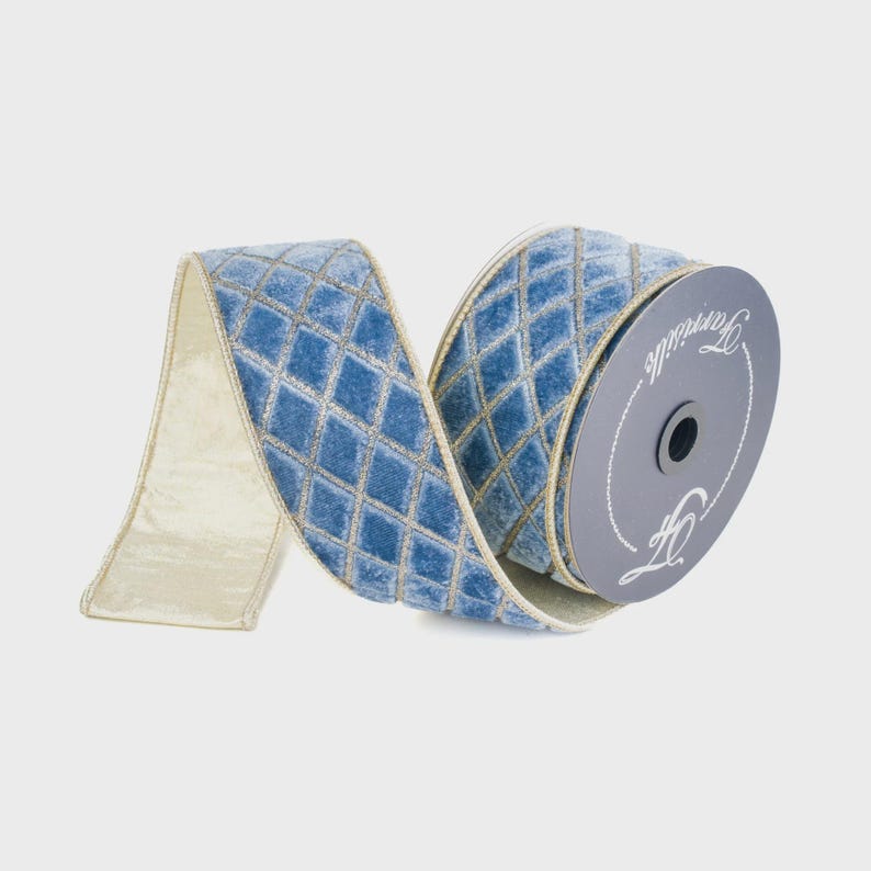 May include: A spool of light blue velvet ribbon featuring a gold diamond lattice pattern. The ribbon has a solid light blue velvet underside and is wound around a grey circular cardboard core with the brand name Farrisilk printed in white.