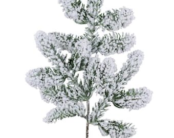 May include: A single artificial evergreen branch with a dusting of white snow. The green needles are visible beneath the snow, and the stem is a muted brown. This decorative piece is ideal for holiday and winter decor.