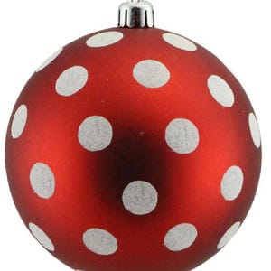 May include: A red Christmas ornament with white polka dots. The ornament has a matte finish and a silver metal cap for hanging. This festive decoration is perfect for adding a touch of holiday cheer to any Christmas tree.