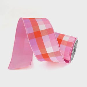 May include: A roll of pink ribbon with a plaid pattern in shades of pink, orange, and white. The ribbon is made of a smooth, silky material and is ideal for crafting, gift wrapping, or decorating.