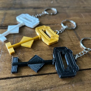 May include: Three key-shaped keychains in black, gold, and white. Each keychain features a unique design with a keyhole and a diamond-shaped handle.
