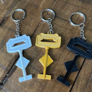May include: Three key-shaped keychains in white, gold, and black. Each keychain has a unique design and is attached to a silver metal ring.