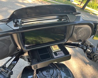 Puede incluir: Panel de instrumentos de motocicleta negro con una pantalla grande, altavoces y un compartimento de almacenamiento. El compartimento contiene un teléfono, un encendedor y otros objetos pequeños. La motocicleta está estacionada en una calle.