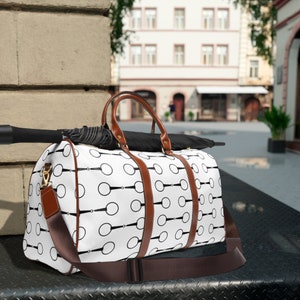 May include: A white and brown travel duffel bag with a black and white geometric pattern. The bag has a brown leather strap and a black handle.