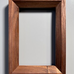May include: A rectangular wooden picture frame with a rich, dark brown finish. The frame has a simple, classic design with clean lines and a beveled edge, perfect for displaying photos or artwork.