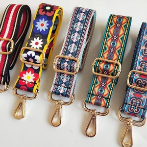 May include: Five colorful patterned bag straps with gold-tone metal hardware. Designs include stripes, floral, and geometric patterns in red, black, yellow, blue, and teal. Each strap has a gold-tone metal clasp.