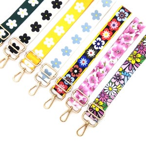 May include: A selection of floral patterned bag straps with gold-coloured metal hardware. The straps display various flower designs in shades of green, white, yellow, blue, red, pink, and purple. Each strap is approximately 2.5 cm wide.