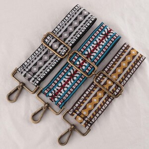 May include: Three decorative bag straps with brass-colored hardware. The straps feature woven patterns in various colors: black, gray, and white; blue, red, and white; and brown, yellow, and white. Each strap has a metal clasp for attachment.