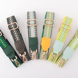 Op de afbeelding: Zes kleurrijke geweven tasriemen in groen, grijs en geel. Elke riem heeft goudkleurige metalen hardware, waaronder verstelbare gespen en draaibare sluitingen, en een imitatie leren eindstuk.